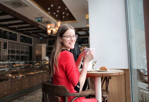 Free A smiling woman in a red sweater enjoys coffee at a cozy indoor cafe. Stock Photo
