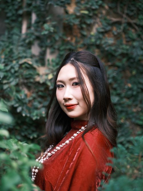 Free Portrait of a woman in a red traditional dress, surrounded by lush greenery. Stock Photo