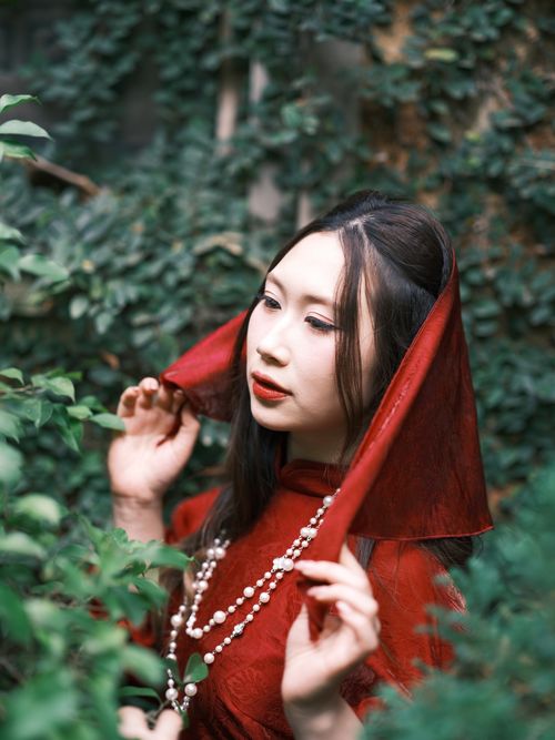Free Capture of a woman in a traditional red Ao Dai, surrounded by lush greenery in Vietnam. Stock Photo