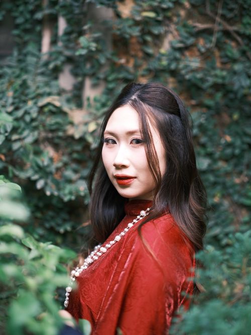 Free Beautiful portrait of a woman wearing a red dress in a lush green outdoor setting. Stock Photo