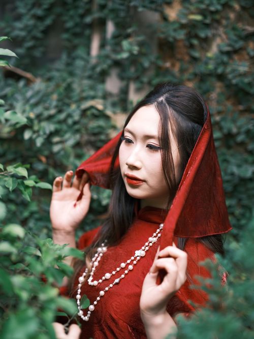Free Portrait of Vietnamese woman in red Ao Dai, surrounded by greenery, exuding elegance and tradition. Stock Photo