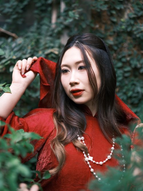 Free Vietnamese woman in red ao dai posing gracefully outdoors among foliage. Stock Photo