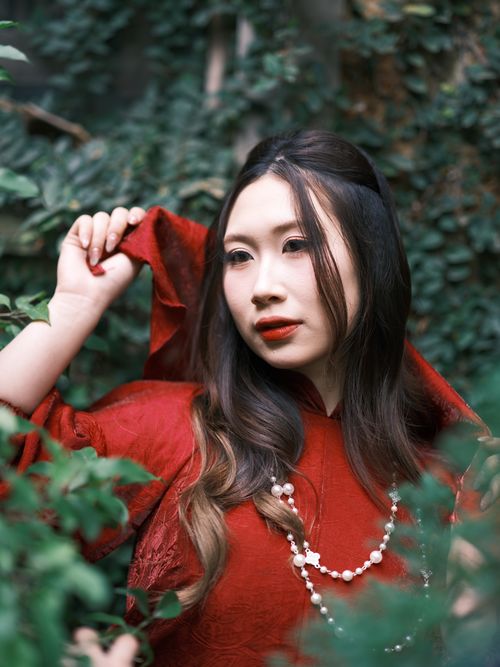 Free A sophisticated woman wearing a red dress surrounded by lush greenery. Stock Photo