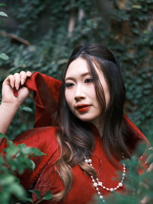 Free Elegant portrait of a young woman in red traditional dress amidst greenery. Stock Photo