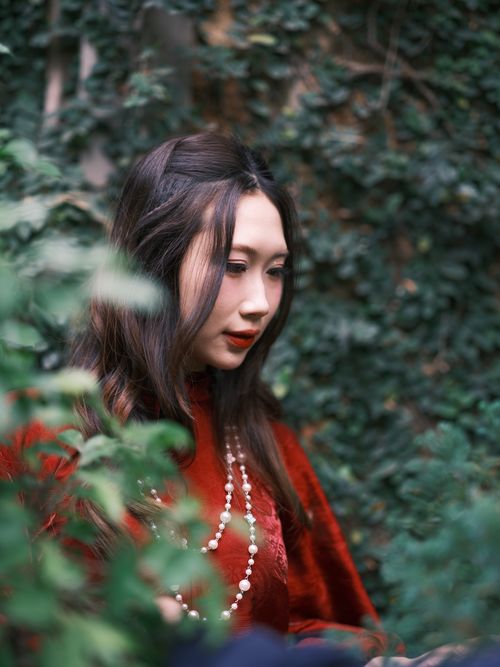 Free A serene portrait of a woman in red traditional attire surrounded by lush greenery. Stock Photo