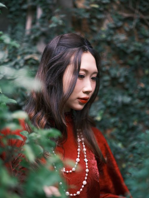 Free Portrait of a woman in a red dress with pearls, surrounded by lush greenery in Việt Nam. Stock Photo