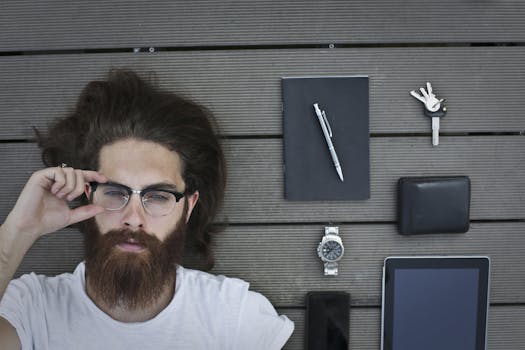 Portrait of a bearded man lying on wood decking with gadgets and accessories.