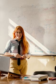 A smiling teacher in a classroom setting, standing near a whiteboard, embodying a positive and engaging learning environment.