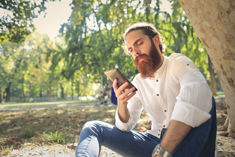 Man In White Dress Shirt And Blue Denim Jeans Sitting On Ground