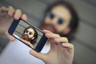 一个留着胡子的男子在户外戴着太阳镜用智能手机自拍