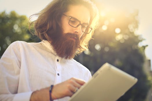 一个阳光明媚的日子里，一个留着胡子的男人在户外全神贯注地使用电子平板电脑