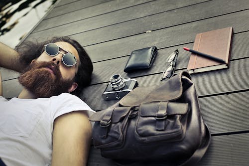 Man in White Crew Neck T-shirt Wearing Sunglasses Lying on Black wooden surface