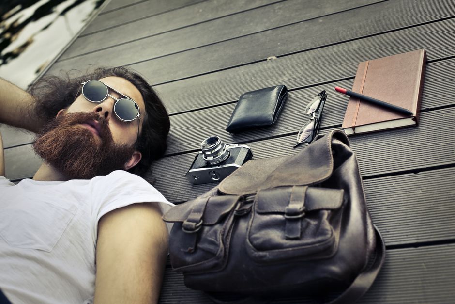 A young bearded man relaxing with sunglasses and accessories like a camera, wallet, and bag. A young bearded man relaxing with sunglasses and accessories like a camera, wallet, and bag.
