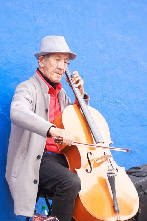 Free Elderly man playing cello against vibrant blue wall in Bogotá, Colombia. Stock Photo
