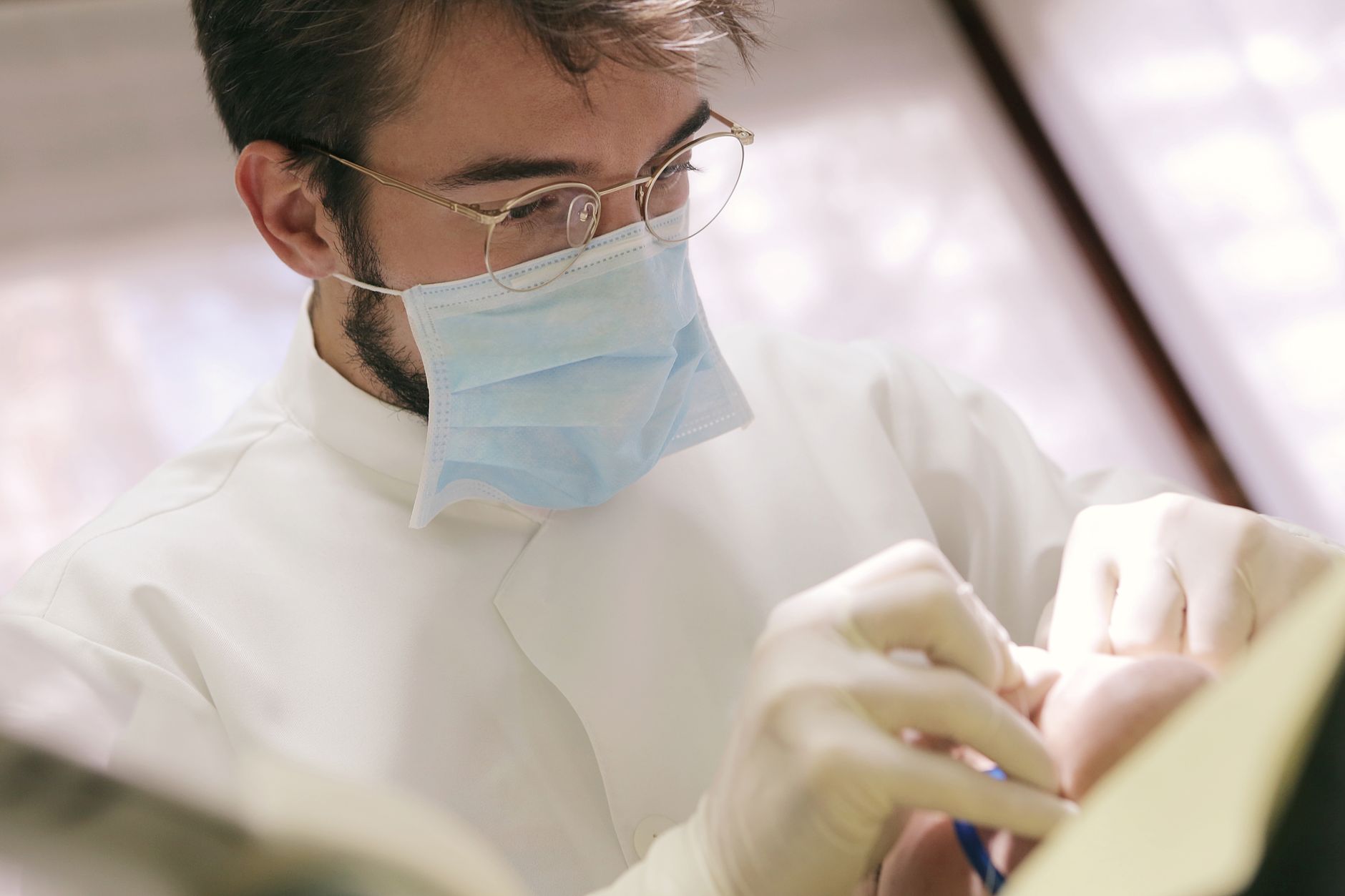Close-up of dentist wearing face mask and gloves performing a procedure on a patient in a clinic.