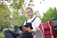 晴朗的日子里，年轻人悠闲地坐在公园长凳上使用平板电脑