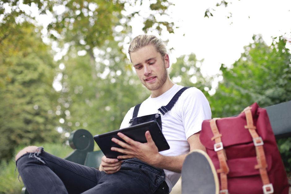Casual young man sitting on a park bench using a tablet during a bright day. Casual young man sitting on a park bench using a tablet during a bright day.
