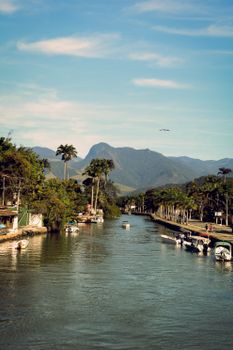A tranquil summer view of a canal in Rio de Janeiro, surrounded by lush greenery and boats.