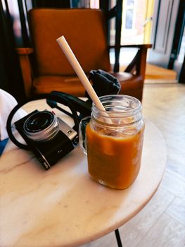Warm café interior with an iced coffee in a mason jar and a vintage camera on a marble table.