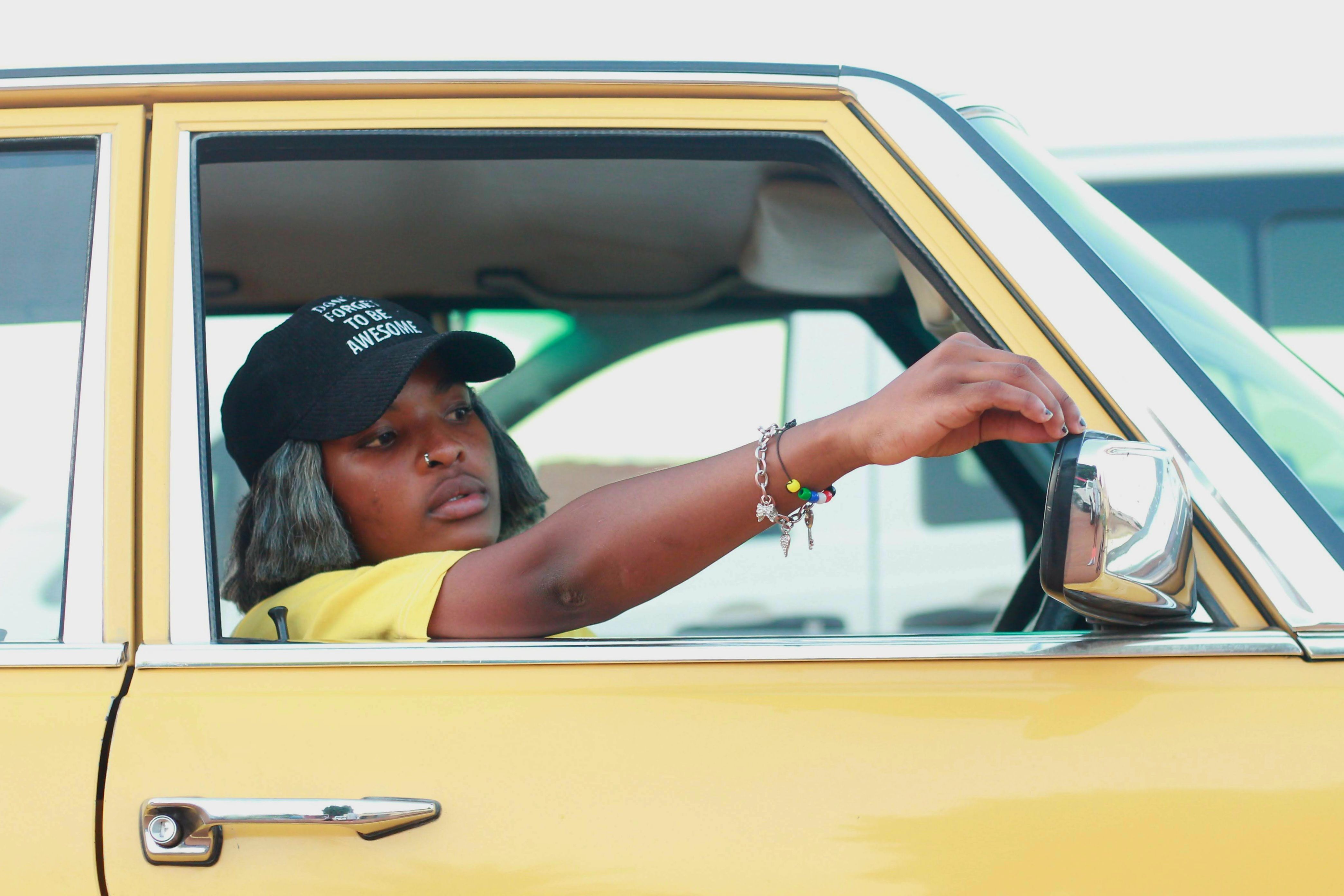 A young woman adjusts the side mirror of a vintage yellow car in Soweto, South Africa