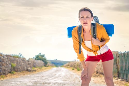 Free A young woman with a backpack pauses on a rural dirt road while hiking outdoors on a bright sunny day. Stock Photo