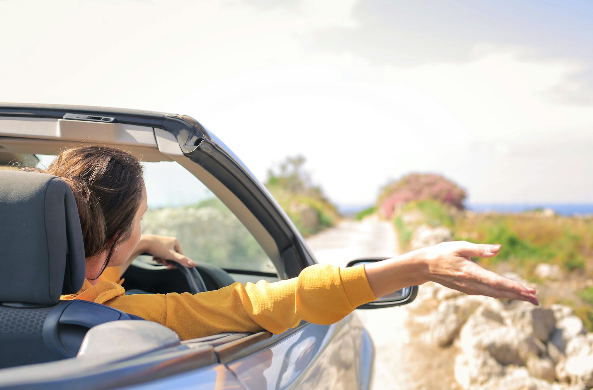 A woman in a convertible car enjoys a carefree summer drive along a scenic coastal road.