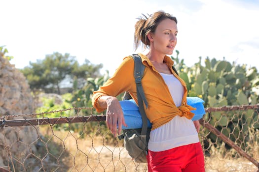 Woman enjoying a summer day outside, leaning on a fence with a backpack.