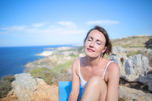 Free A woman relaxes with closed eyes on a scenic seaside cliff, embracing the warmth of summer. Stock Photo