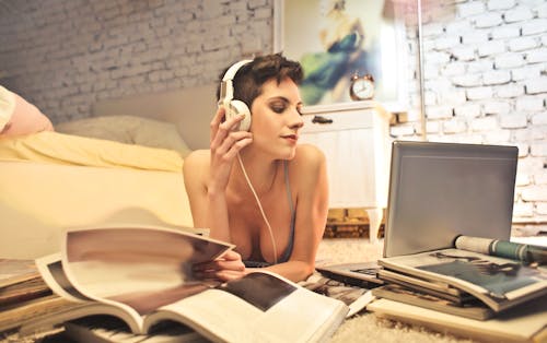 Woman Wearing Headphone Beside Magazines