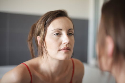 A woman thoughtfully looking at herself in a bathroom mirror.