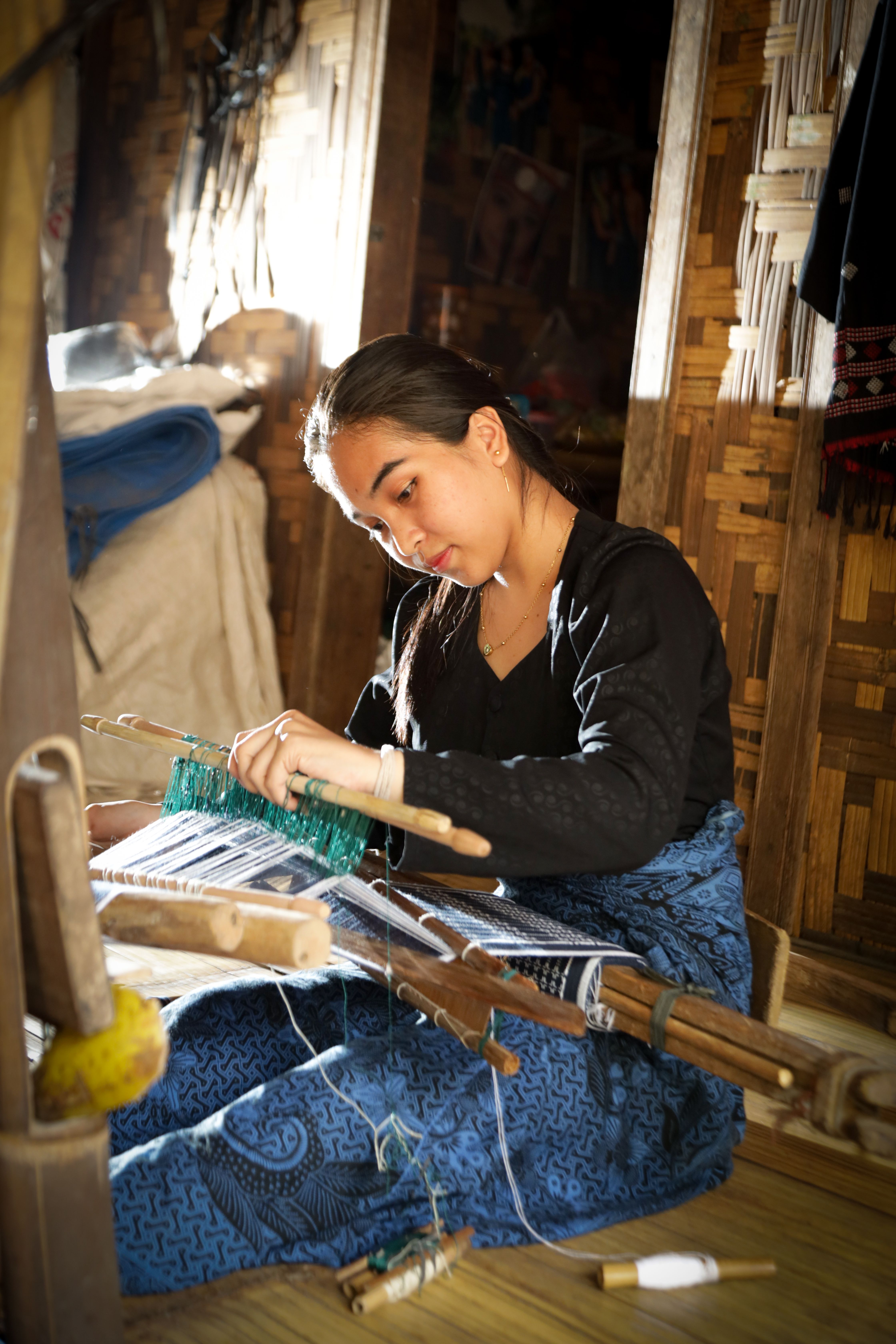 A young woman skillfully weaving traditional fabric on a loom.