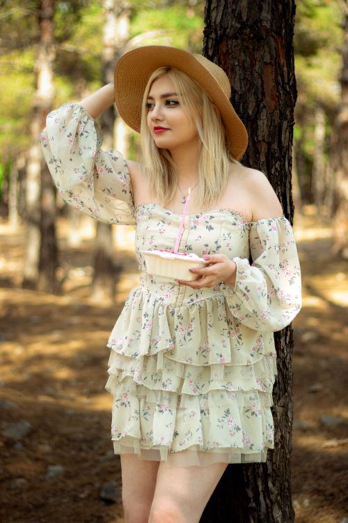 Free Blonde woman wearing a floral dress and straw hat enjoying a summer day in the woods. Stock Photo