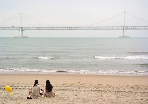 Two women sitting on Gwangalli Beach near Gwangandaegyo Bridge in Busan, South Korea.