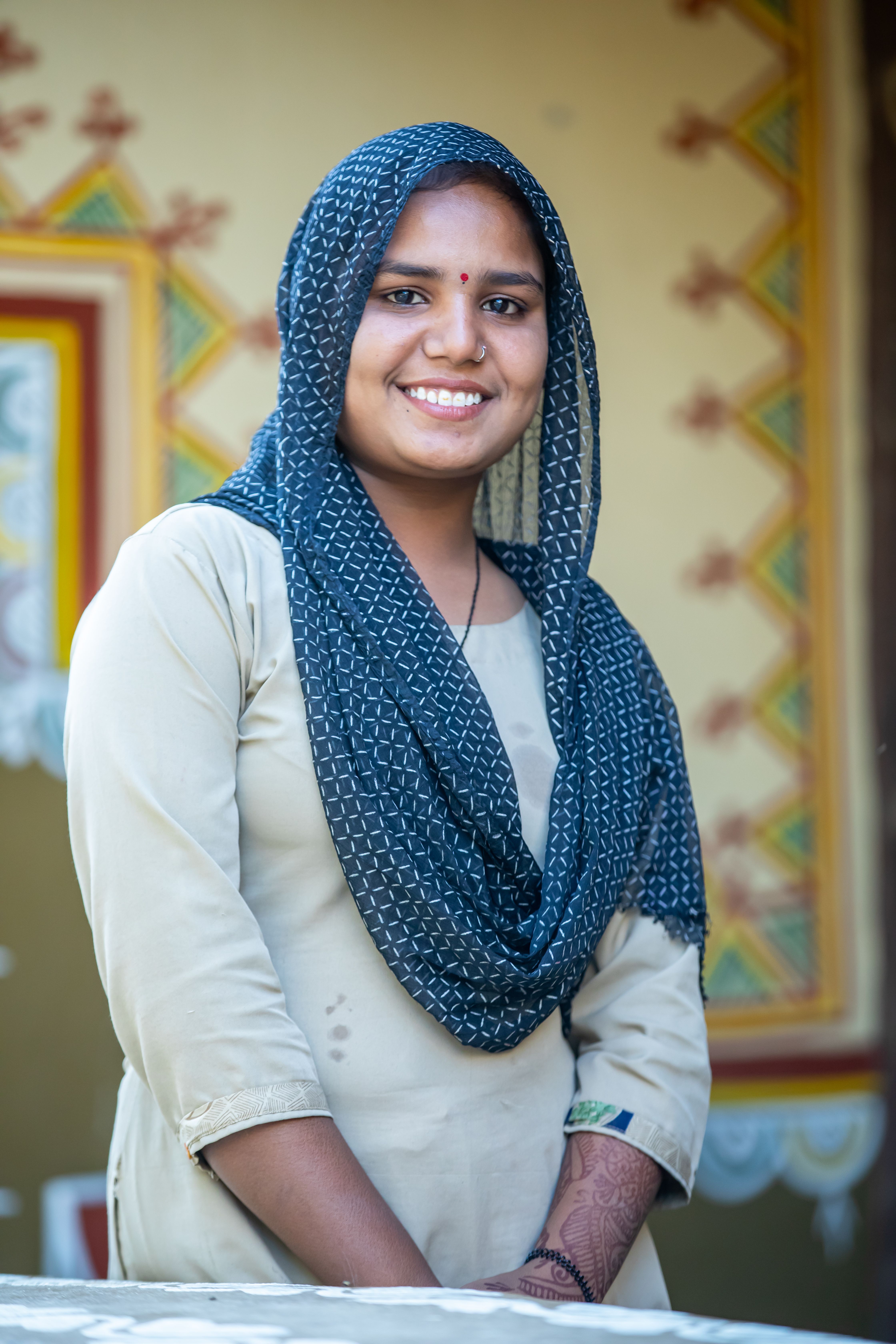 A smiling Rajasthani woman in traditional attire against a cultural backdrop.