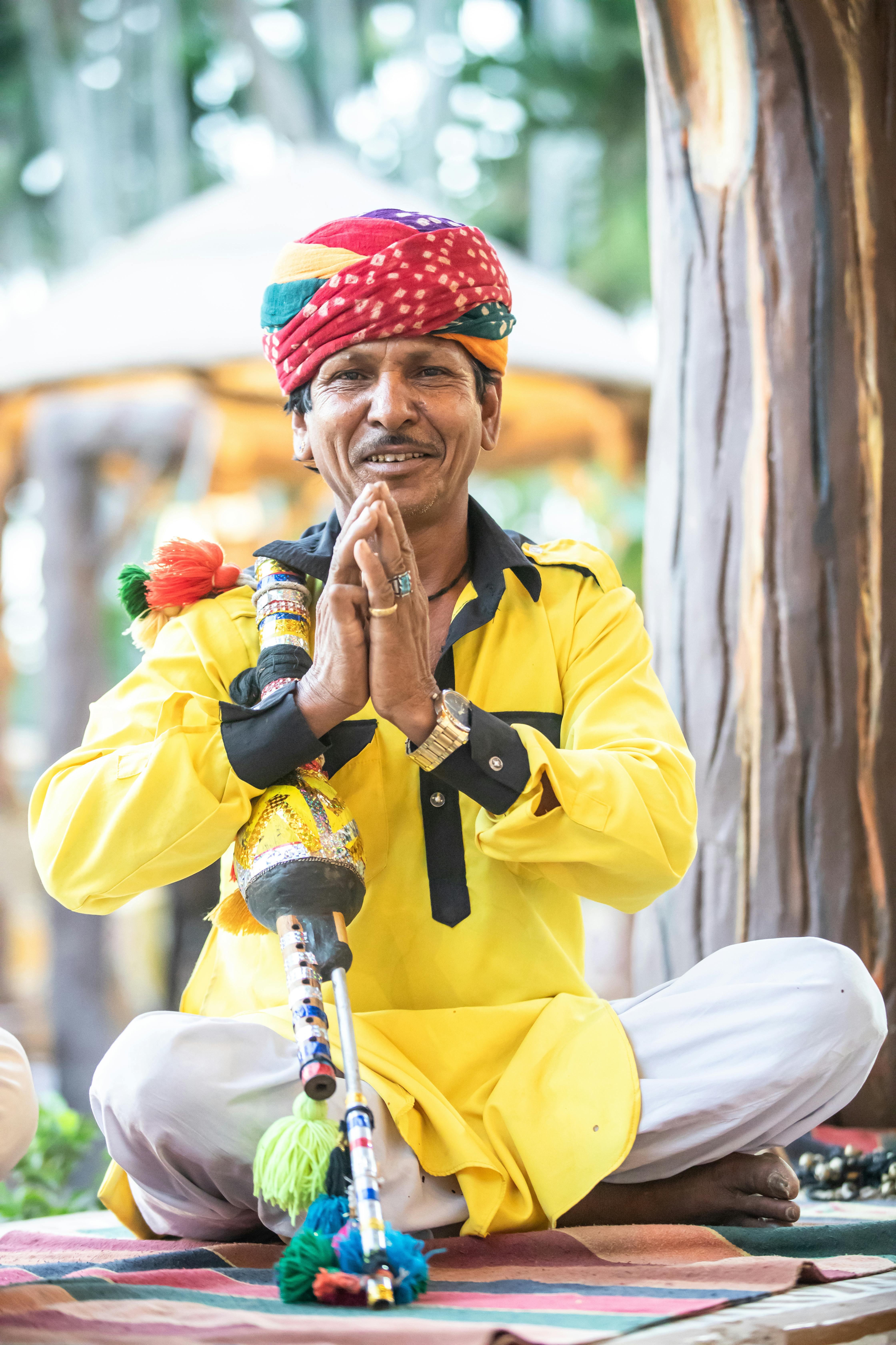 Rajasthani folk musician in traditional attire playing an ethnic instrument. Vibrant cultural scene outdoors.