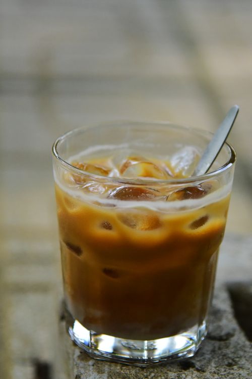 Free A glass of iced coffee with ice cubes and a spoon outdoors on a sunny day. Stock Photo
