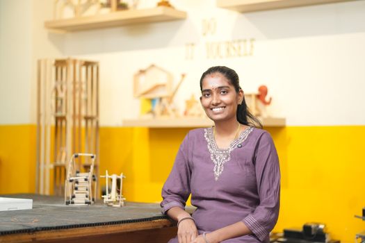 A smiling woman in a purple dress in a DIY workshop setting.