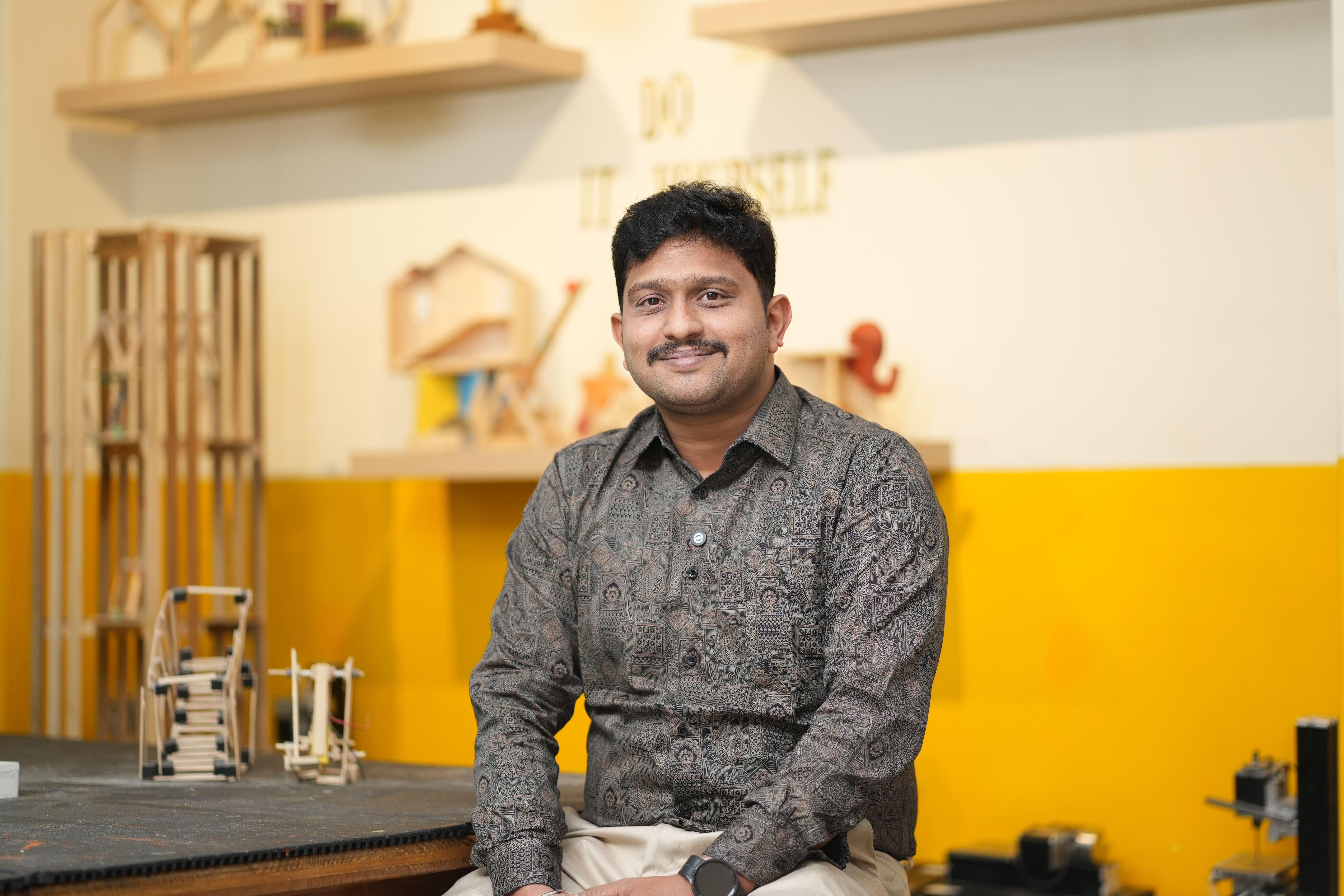 Smiling engineer in an office with wooden prototypes and DIY decor.