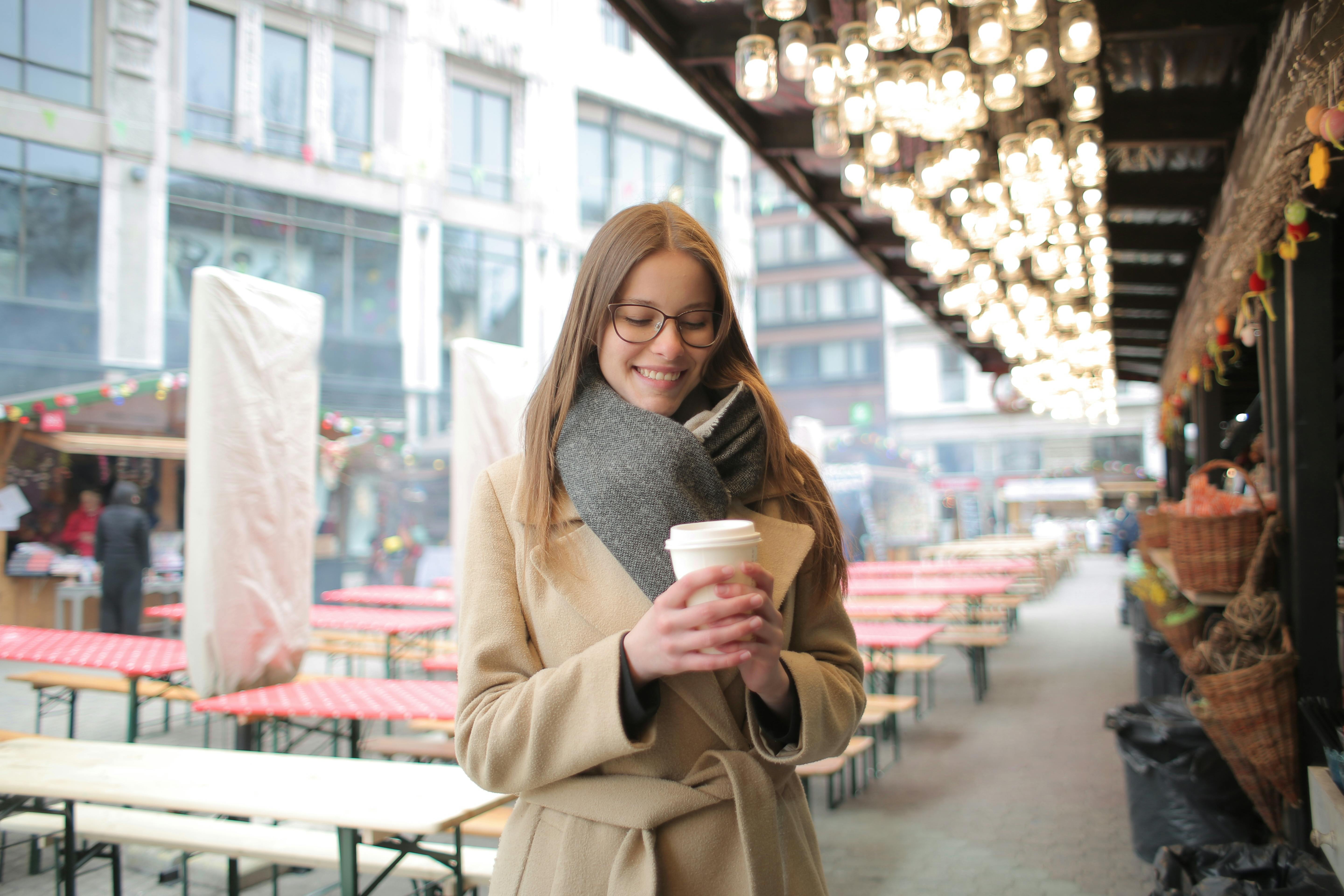 woman in brown coat holding white coffee cup