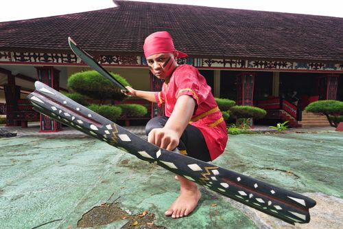 Free A person dressed in traditional Indonesian warrior attire holding swords, striking a pose. Stock Photo