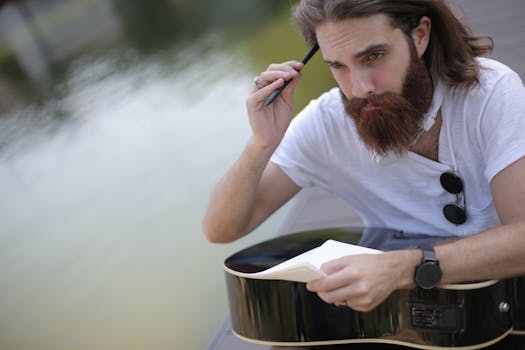 一位音乐家在宁静的水边，带着吉他和笔记本电脑，陷入沉思