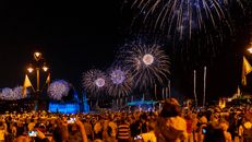 Vibrant night fireworks illuminating Budapest's Parliament and Danube, captivating a large crowd below.