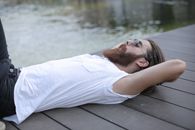 光天化日之下，一名身穿白衬衫、留着胡子的男子悠闲地躺在湖边的码头上
