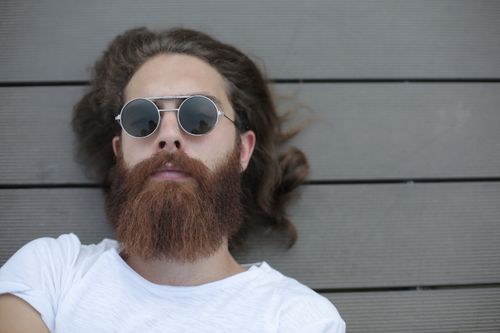 Free Casual portrait of a young man with sunglasses and beard lying on a wooden deck. Stock Photo