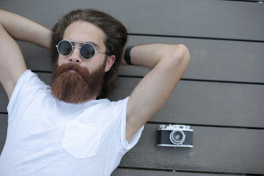 一名留着胡子、戴着太阳镜的男子在户外放松，身旁放着一台模拟相机