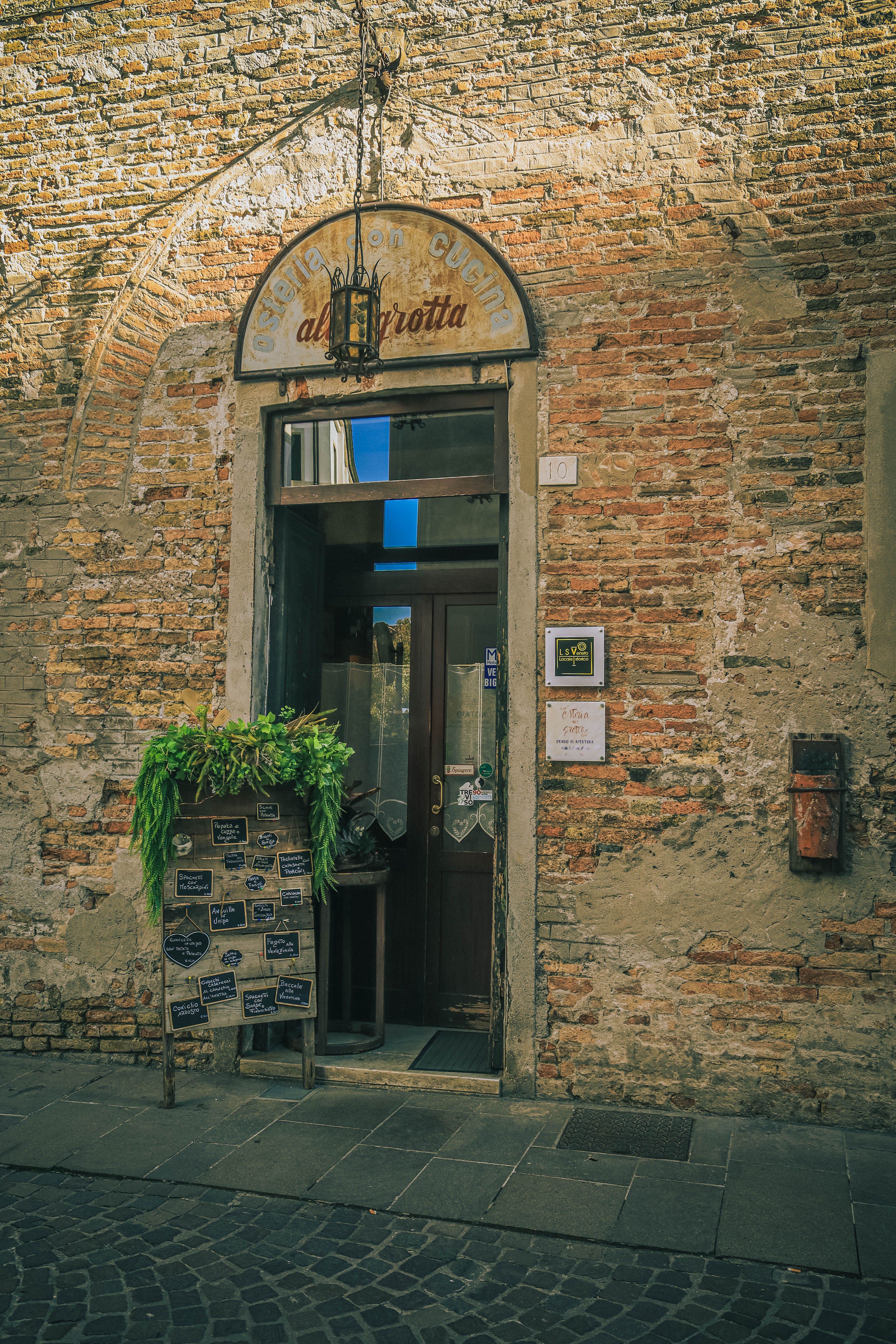 Gratis L'ingresso di un grazioso caffè, con pareti in mattoni rustici e piante verdi, crea un'atmosfera vintage. Foto a disposizione