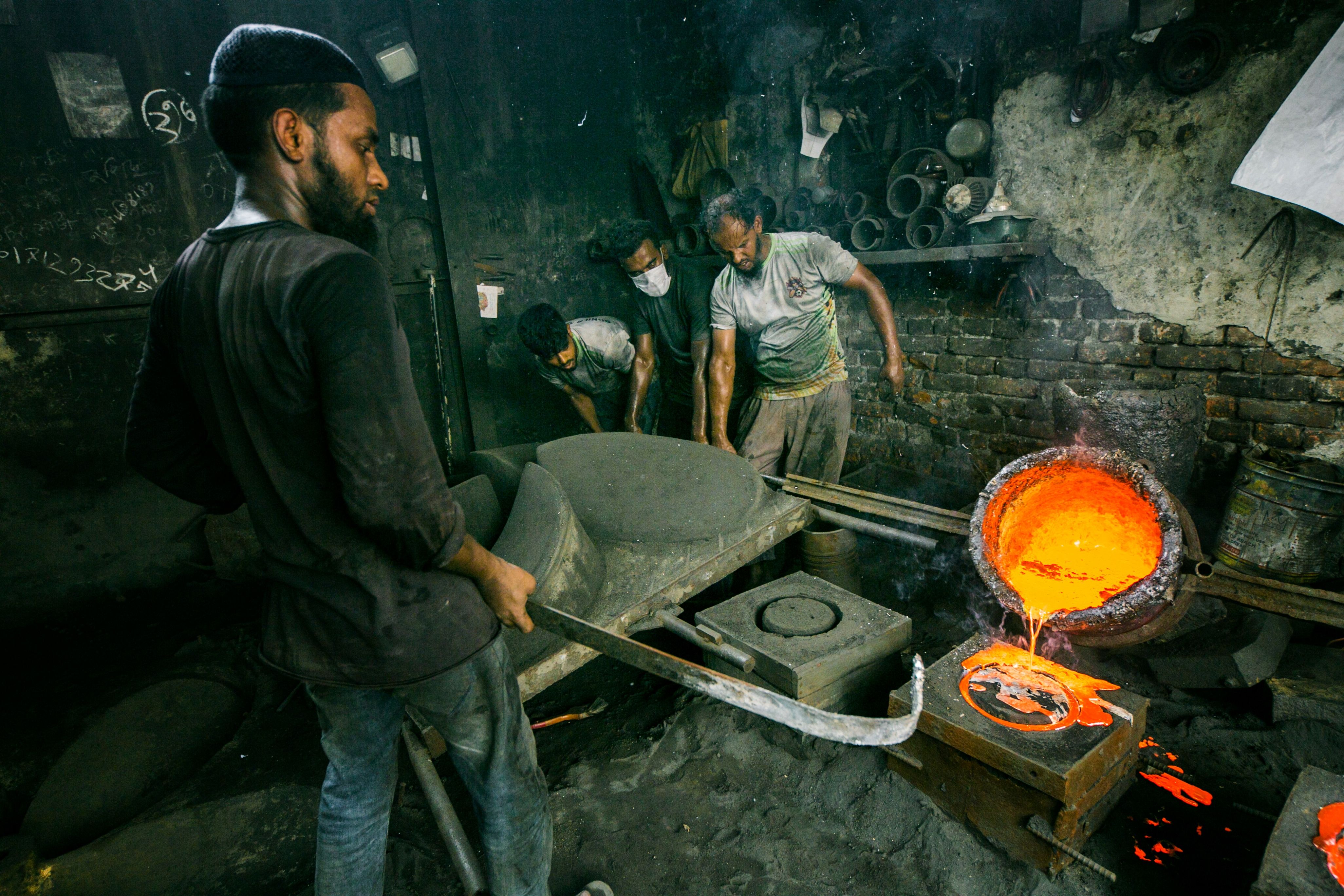 Workers in an industrial foundry pour molten metal into molds, showcasing intense labor and craftsmanship.