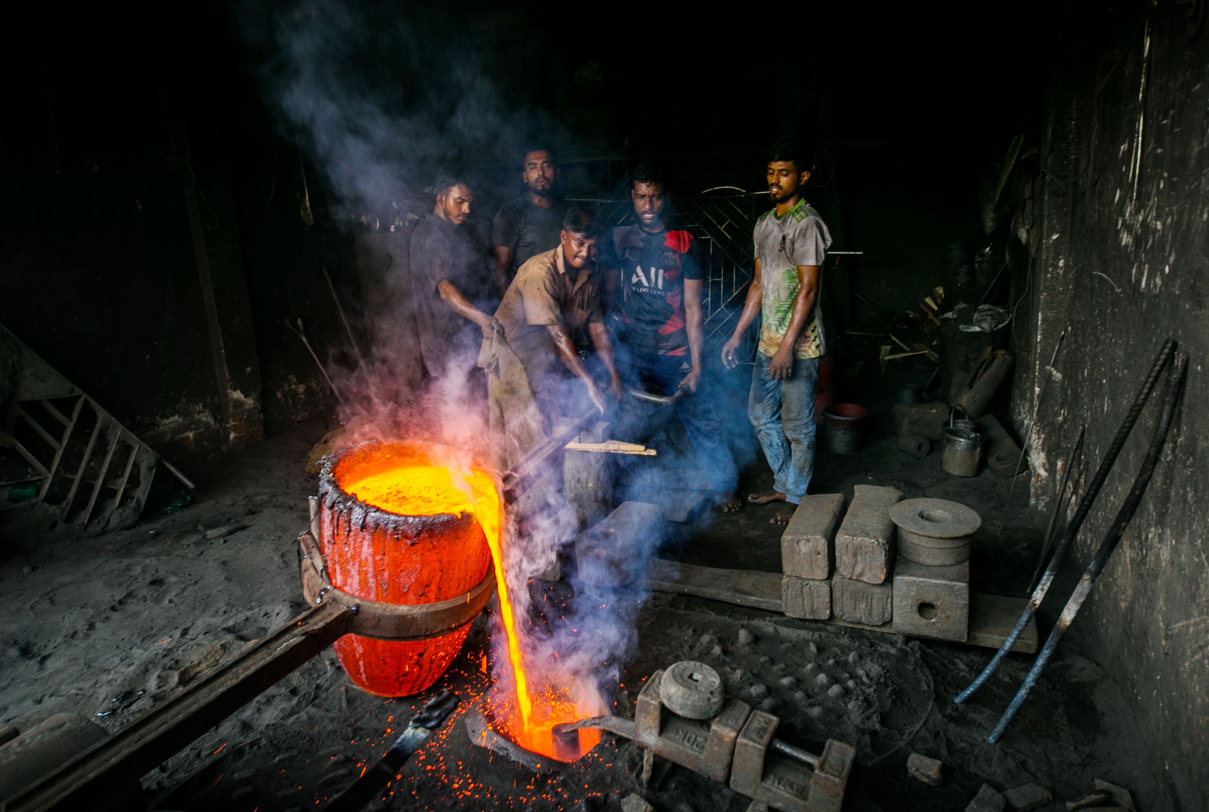 Workers in an industrial foundry safely pouring molten metal from a crucible.