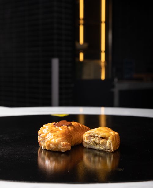 Free Golden flaky pastry with filling on a black reflective surface, artistic indoor food presentation. Stock Photo