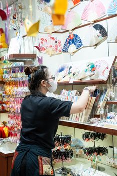 A store employee arranges colorful traditional Japanese fans in a shop.